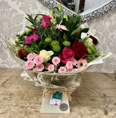 Rosy Dreams Bouquet - A vibrant bouquet with a mix of pink roses, red blooms, and green accents, all wrapped in elegant clear wrap.