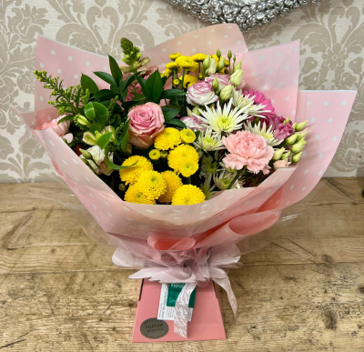 Sweet Surprise - A delightful mix of pinks, yellows, and whites with a touch of greenery, wrapped in soft pink paper for a sweet surprise.